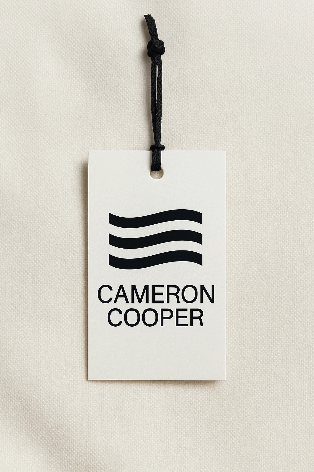A white Cameron Cooper hangtag on a black cord, printed with the three-wave logo